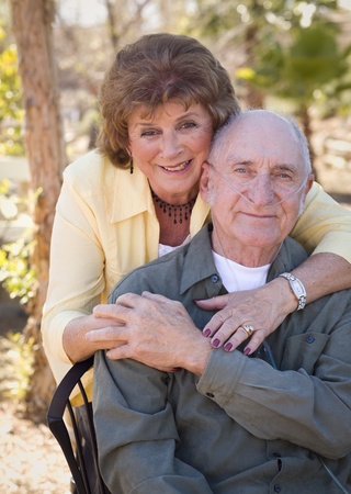 senior woman outside with seated man wearing oxygen tubes.