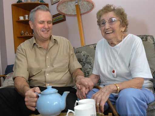 A senior adult woman and her middle aged son enjoy a cup of tea in a living room