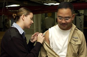 A woman administers a vaccine to a military officer