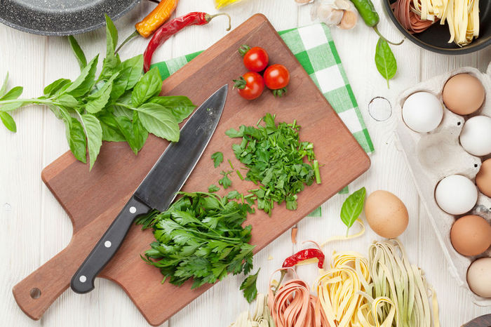 A cutting board with diced greens, tomatoes, chilies, and a carton of eggs