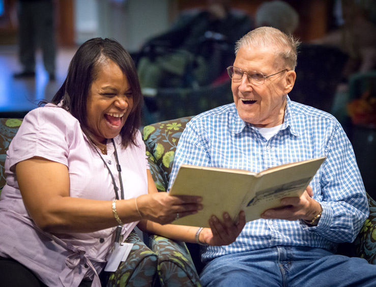 A woman and older man laugh while reading a book together