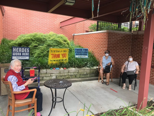 Three women sit outside engaging with each other in an outdoor social distance meeting area.