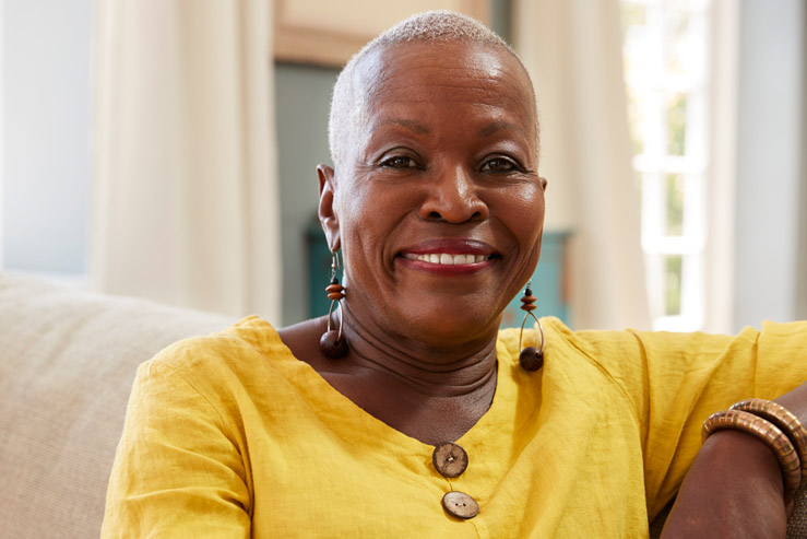 A Black woman with a shaved head and a yellow shirt smiling beautifully