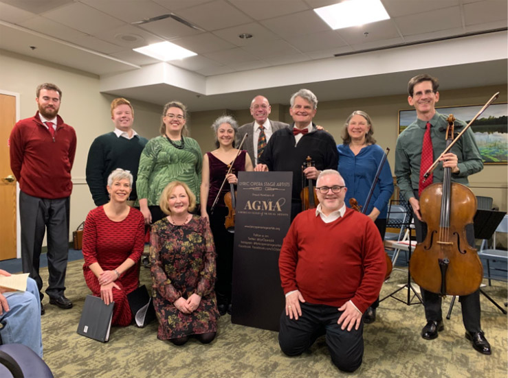 Members of the Lyric Opera Stage Artists pose for a group picture. Most members are wearing dress clothes that is in accordance to a green and red color scheme.