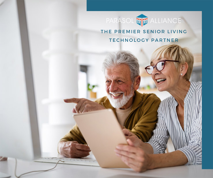 A senior aged male and female couple smile while pointing at something on their computer monitor