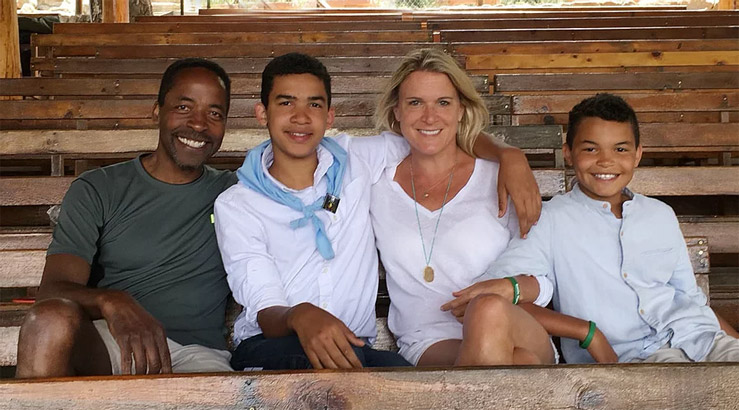 A mixed-race family--a father, mother, and two teenage sons--sits for a photo in front a long aisle of wooden pews.