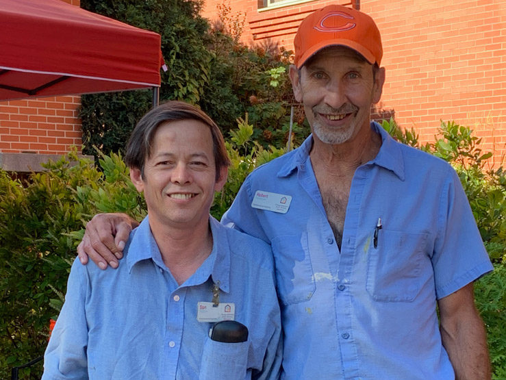 Two men, both dressed in short sleeve button ups smile while gazed toward the viewer.