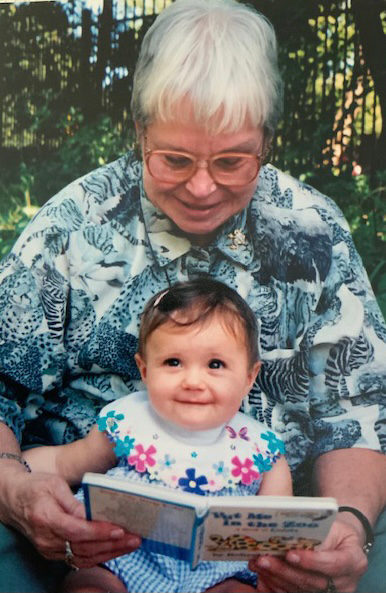 An elderly woman reads a book to her young granddaughter.