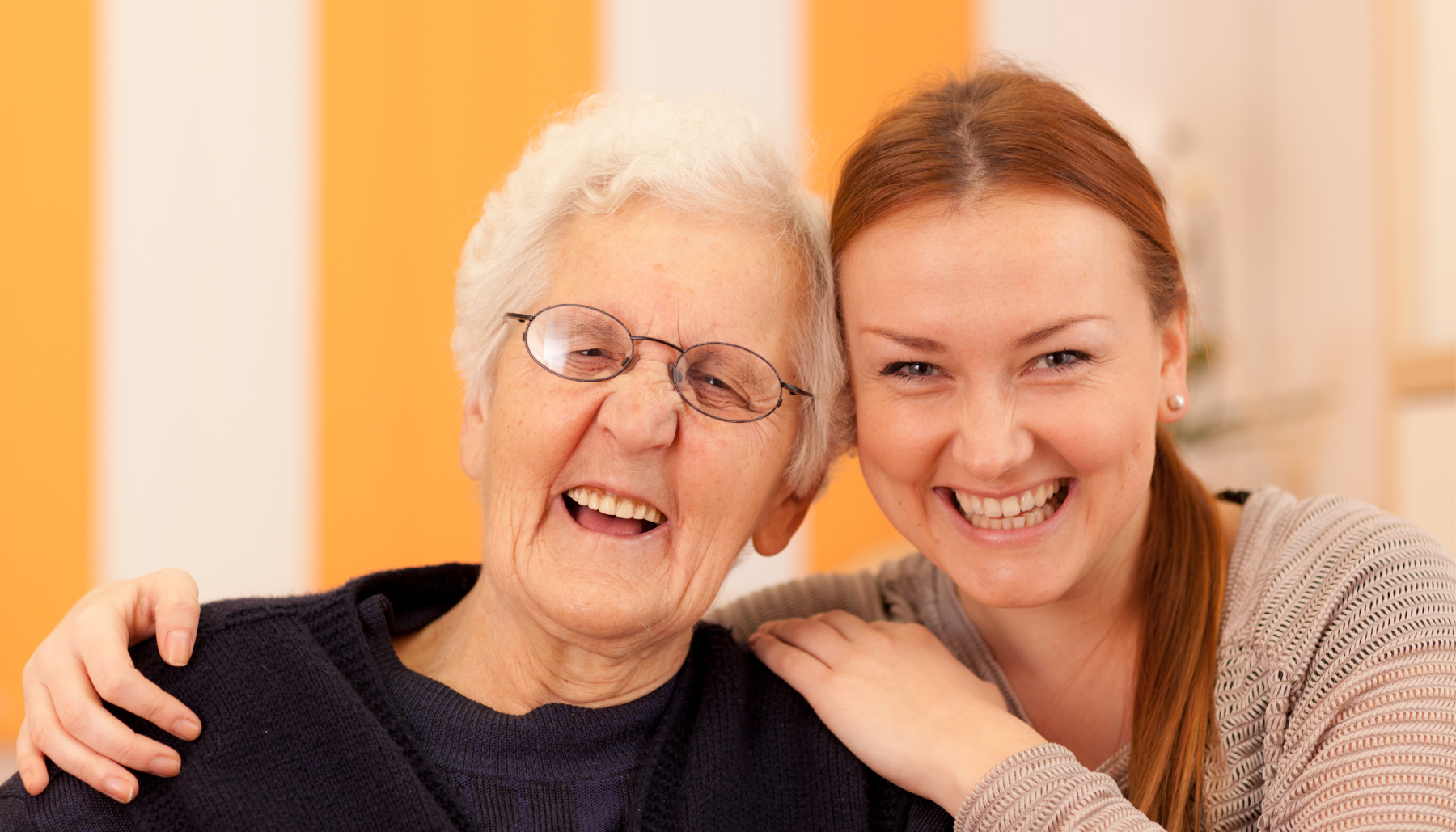 An young woman puts her arm around an older woman, they both are laughing and smiling at the camera.