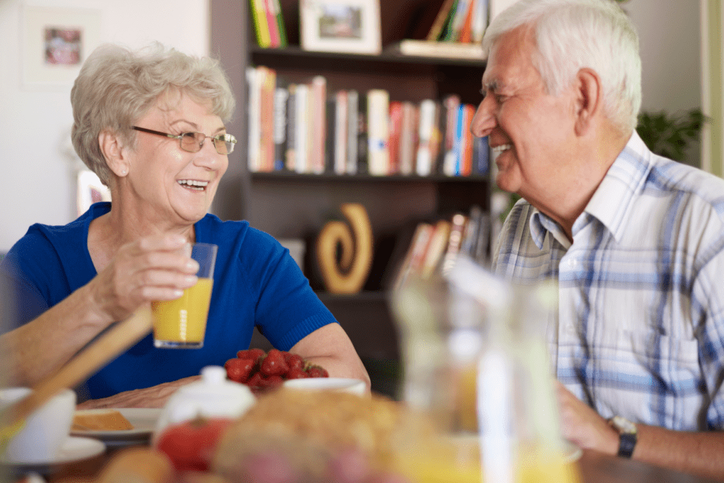 A senior man and senior woman smiling at each other during breakfast.