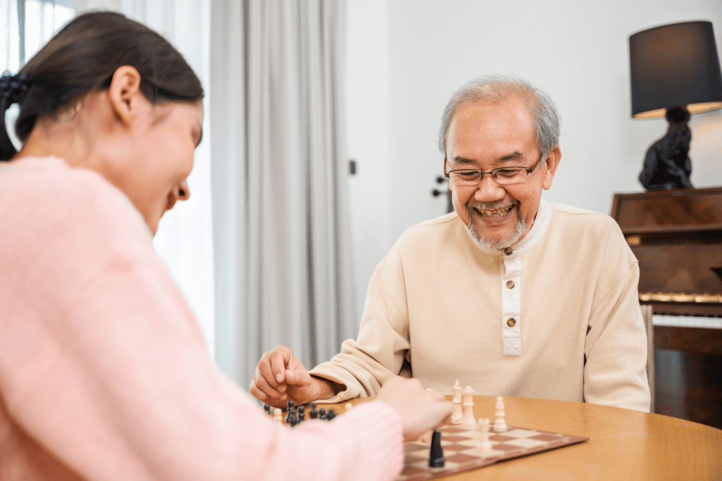 A young woman plays chess with an older man in a beige shirt.