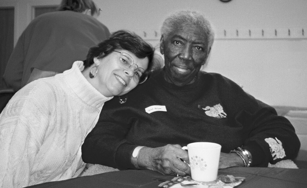 Black and white image of a woman leaning caringly on the should of a older adult woman.