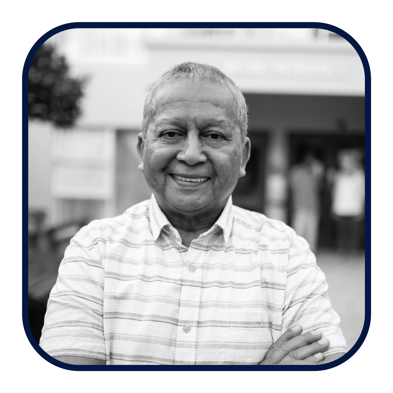 An older man smiles at the camera with his arms crossed in front of his chest.