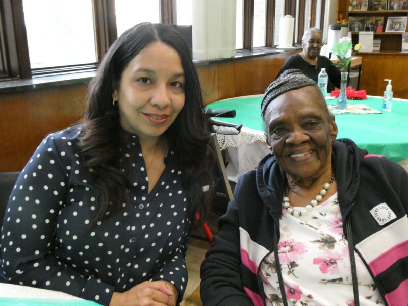 A woman sits next to an older woman and smiles for the camera.