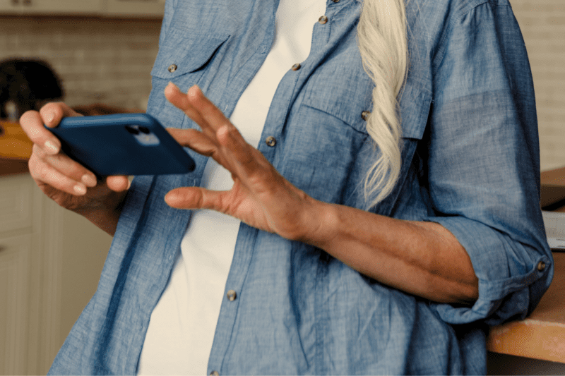 The torso of an older woman with long grey hair as she navigates her cell phone.