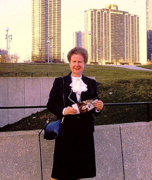 A woman in a chic black outfit poses in front of a skyline.