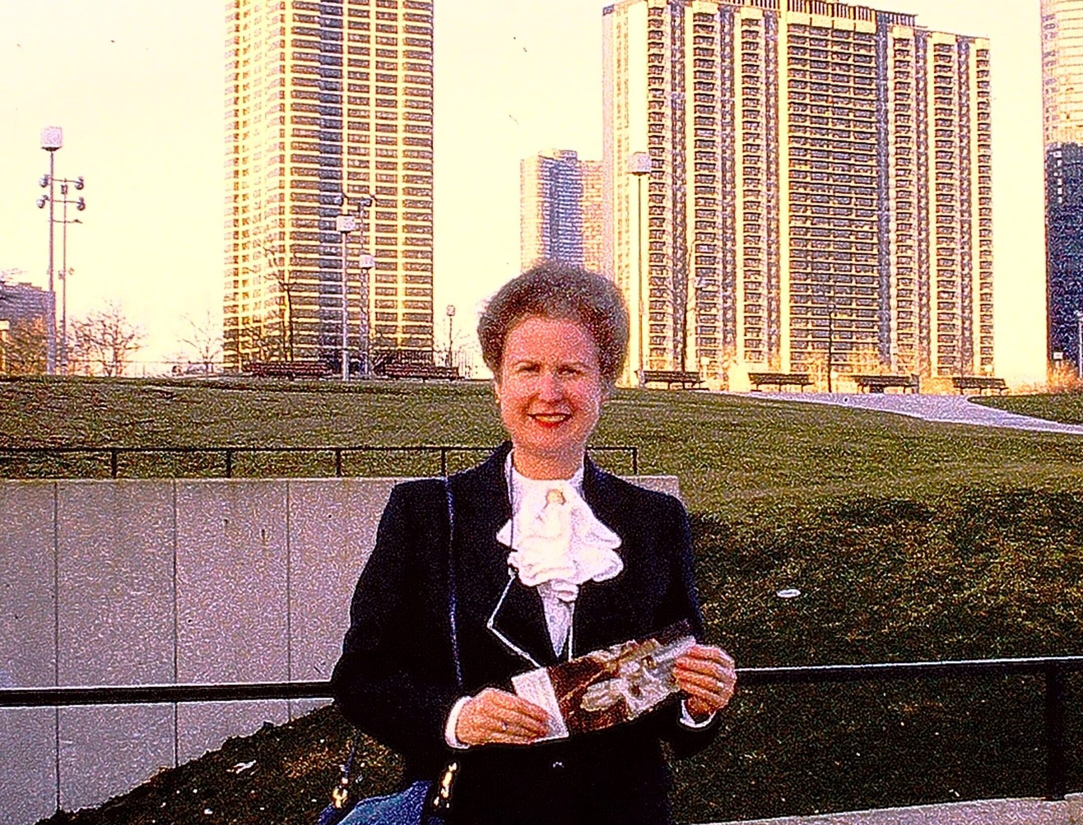 A woman in a chic black outfit poses in front of a skyline.