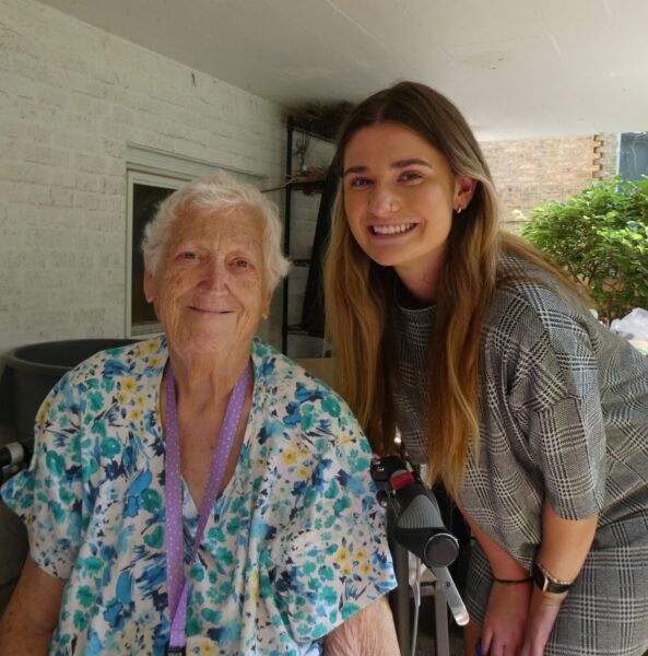 A young woman with long blonde hair crouches next to an older woman in a blue top at an outdoor picnic.