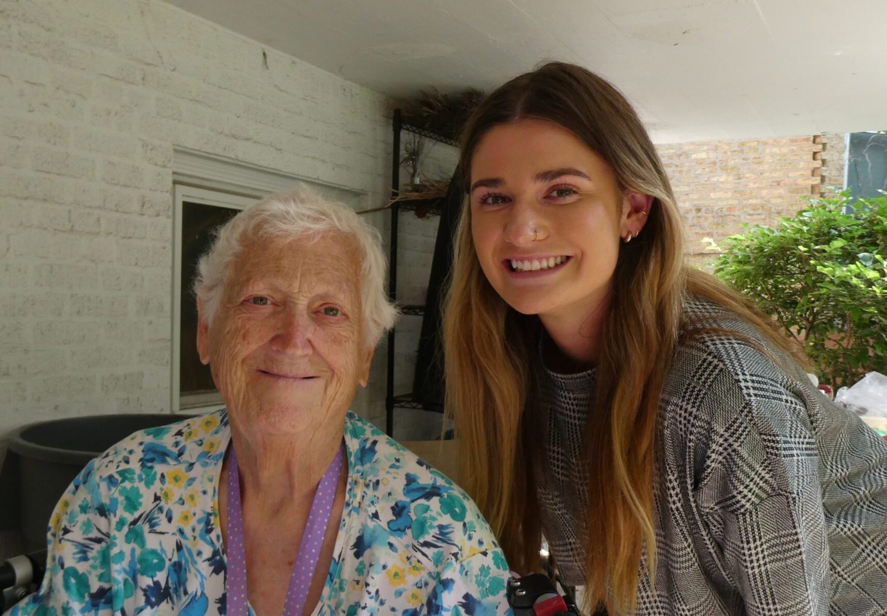 A young woman with long blonde hair crouches next to an older woman in a blue top at an outdoor picnic.