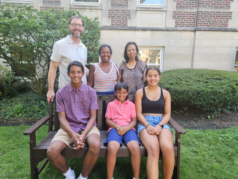 A couple, their three children, and one of their mothers pose on an outdoor bench.