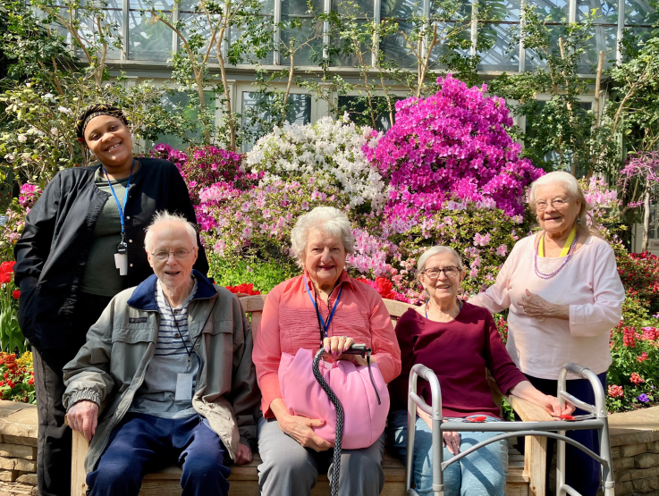 Four Hartwell Place residents and a caregiver pose in front of beautiful pink flowers.