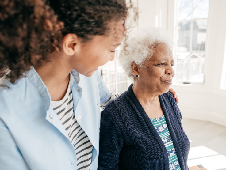 A home care provider helps a senior woman walk by supporting her.