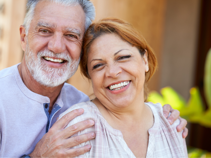 An older man holds his wife by the shoulders and they both smile at the camera.